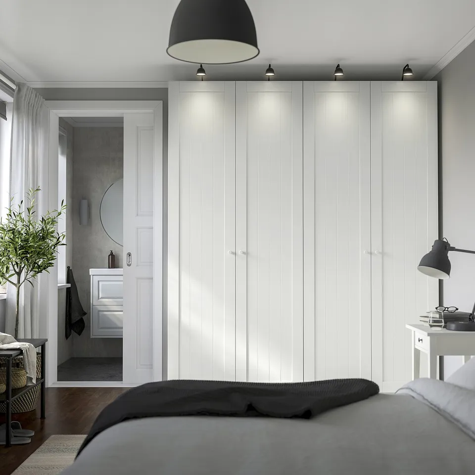 Modern bedroom with tall PAX wardrobes, built-in lighting, and adjacent bathroom door. Grey-bedded foreground.