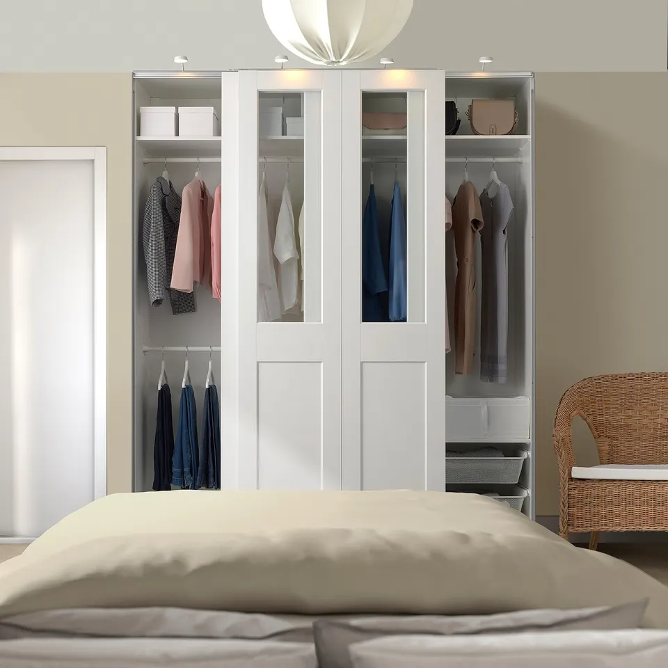 Modern bedroom with large white PAX wardrobe and sliding glass doors. Wicker chair by bed, wardrobe dominates.
