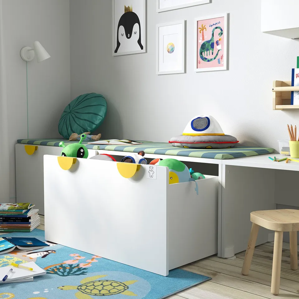 Kids storage bench with openable box, holding toys. Bright, playful room with wall art and rug.