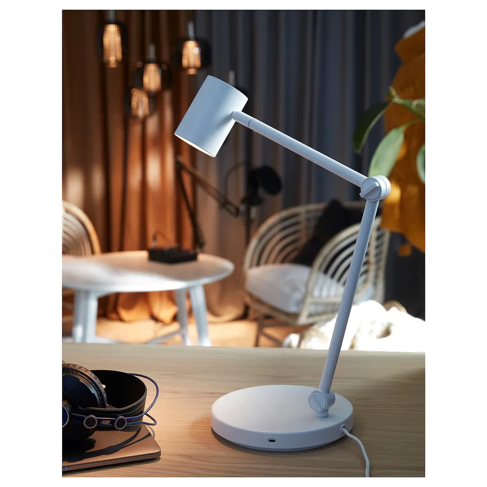 A white NYMÅNE lamp with an adjustable arm and usb port on a wooden desk.