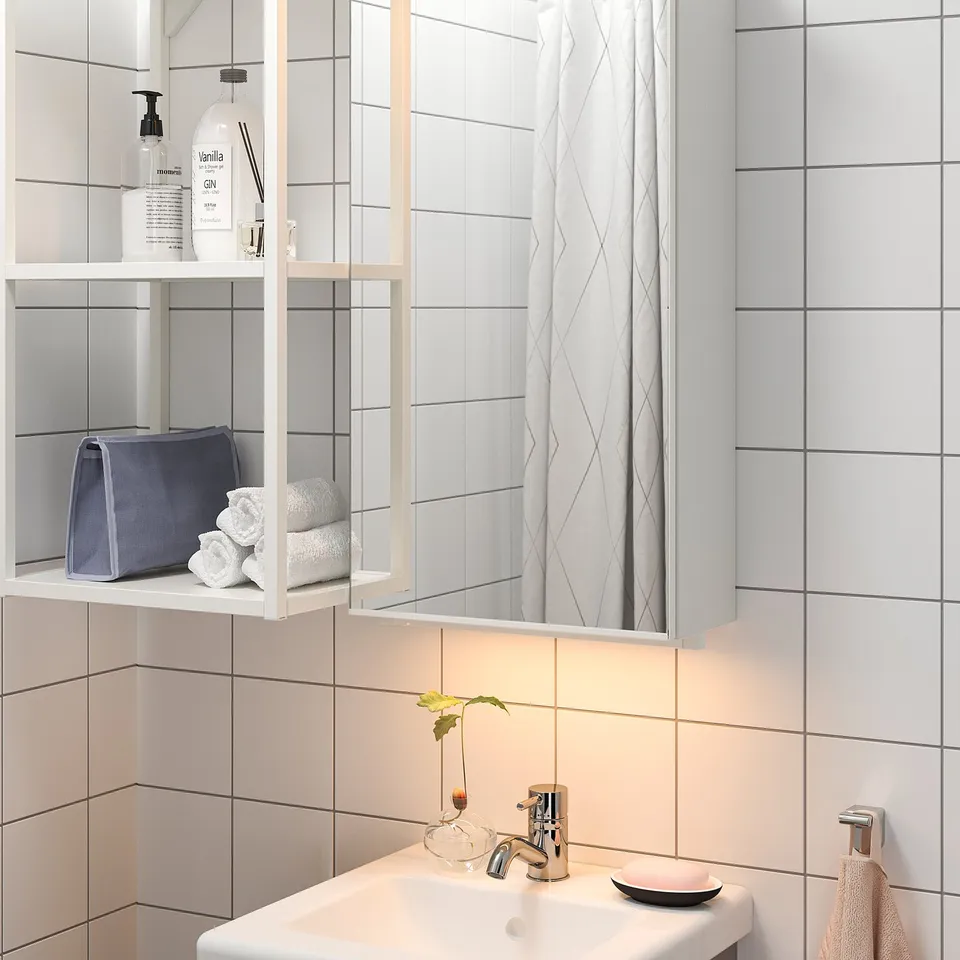 Bathroom with lit mirror cabinet, showing toiletries and towels, with a white sink below.