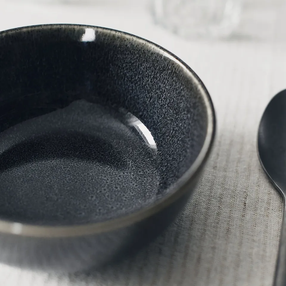Dark grey glazed bowl, smooth finish, resting on a cloth-covered surface.