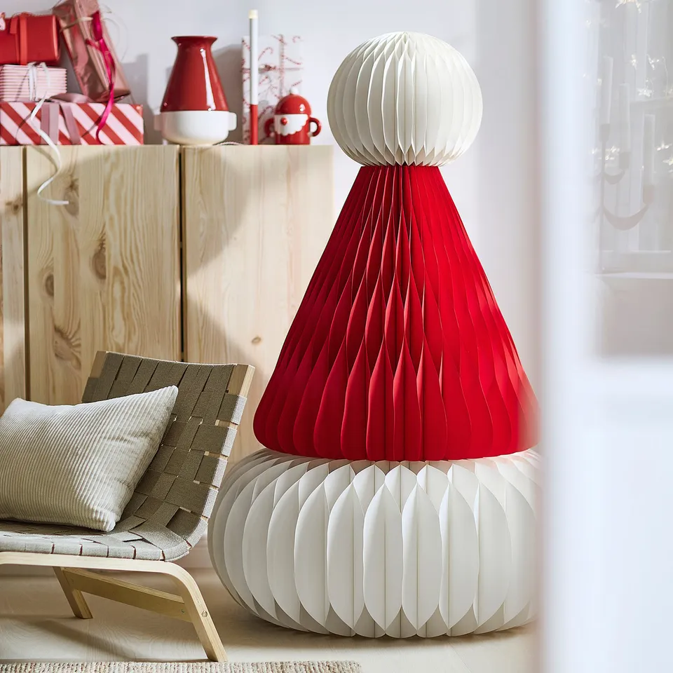 Large red & white paper cone lamp, taller than chair, festive design.