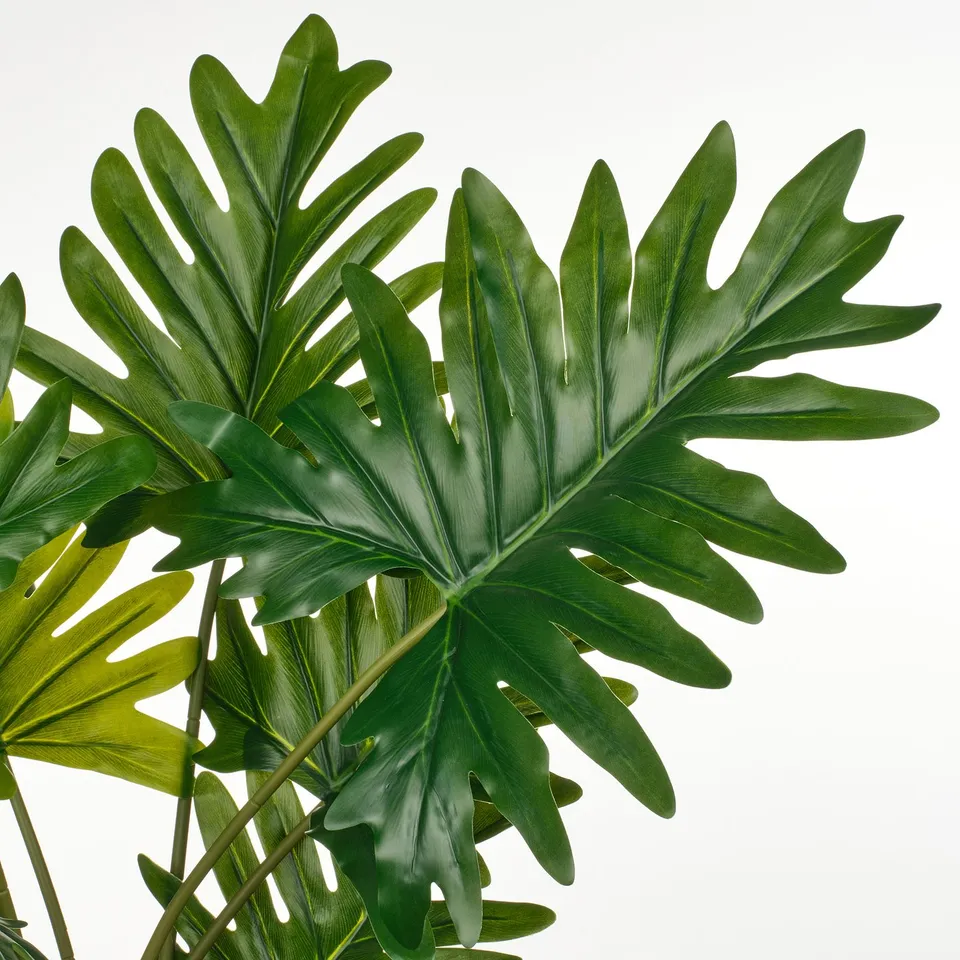 Large green tropical leaves, realistic and vibrant, life-like artificial plant with detailed texture, set against a plain white background.