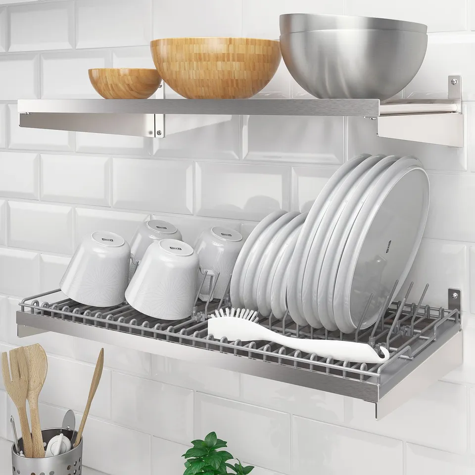 Stainless steel dish drainer mounted on wall, holding white plates and bowls with lids, wooden utensils below.