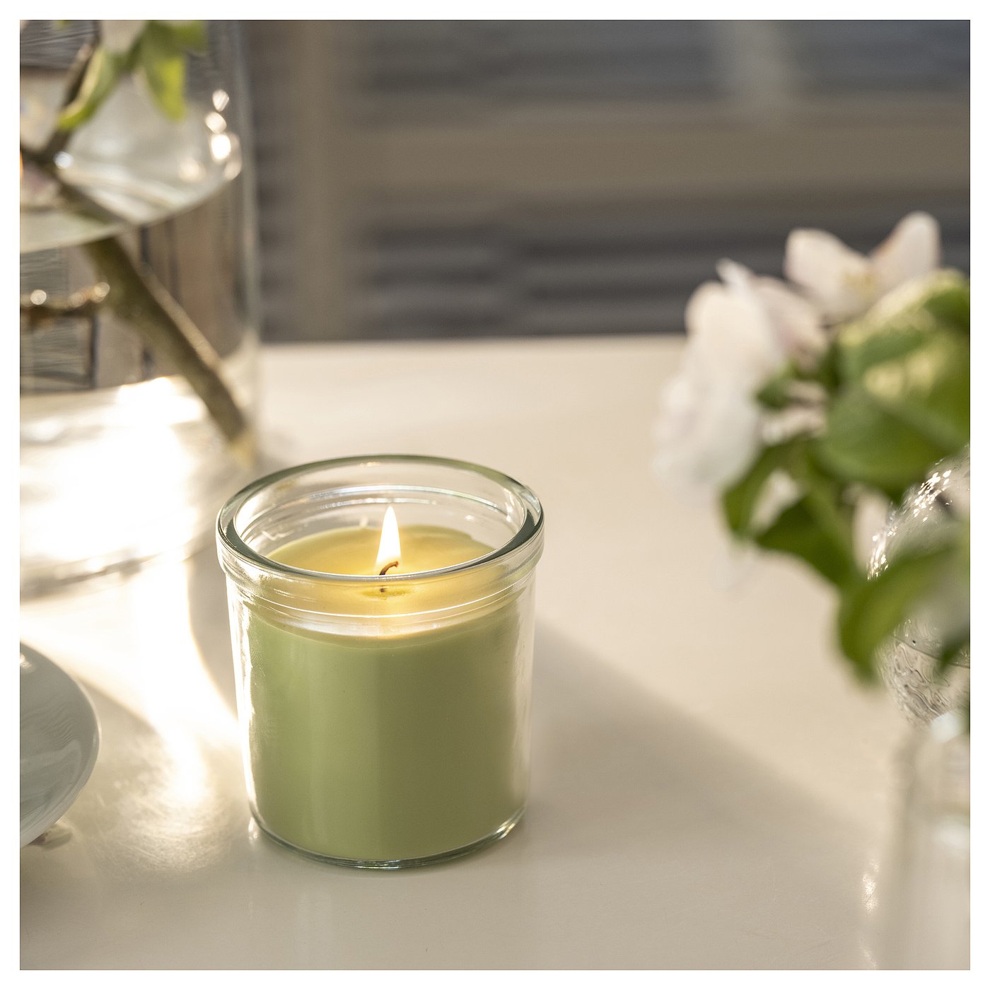 Small green jar candle burning, jasmine-apple scent, fresh home atmosphere.