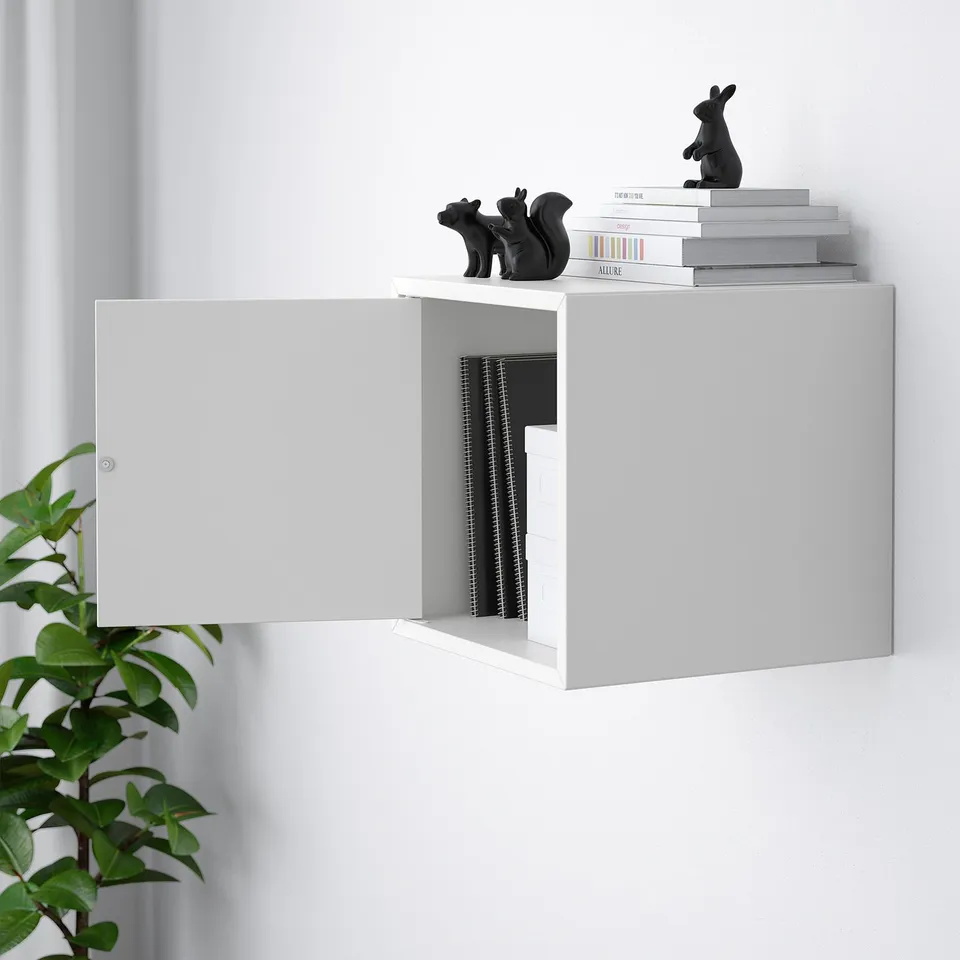White wall-mounted cabinet with open door revealing inner storage, stacked books, and black figurines on top.
