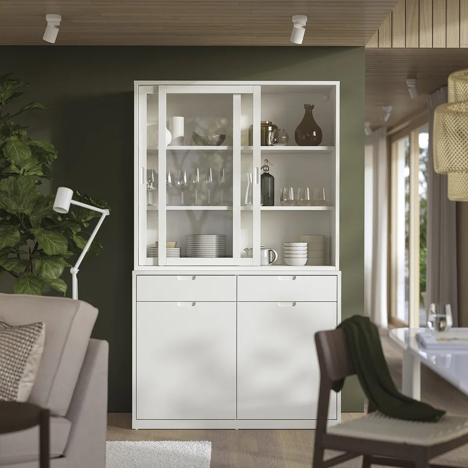 Modern dining area with off-white TONSTAD storage unit, featuring glass doors and soft-close drawers. Holds tableware, with plants and wooden decor.
