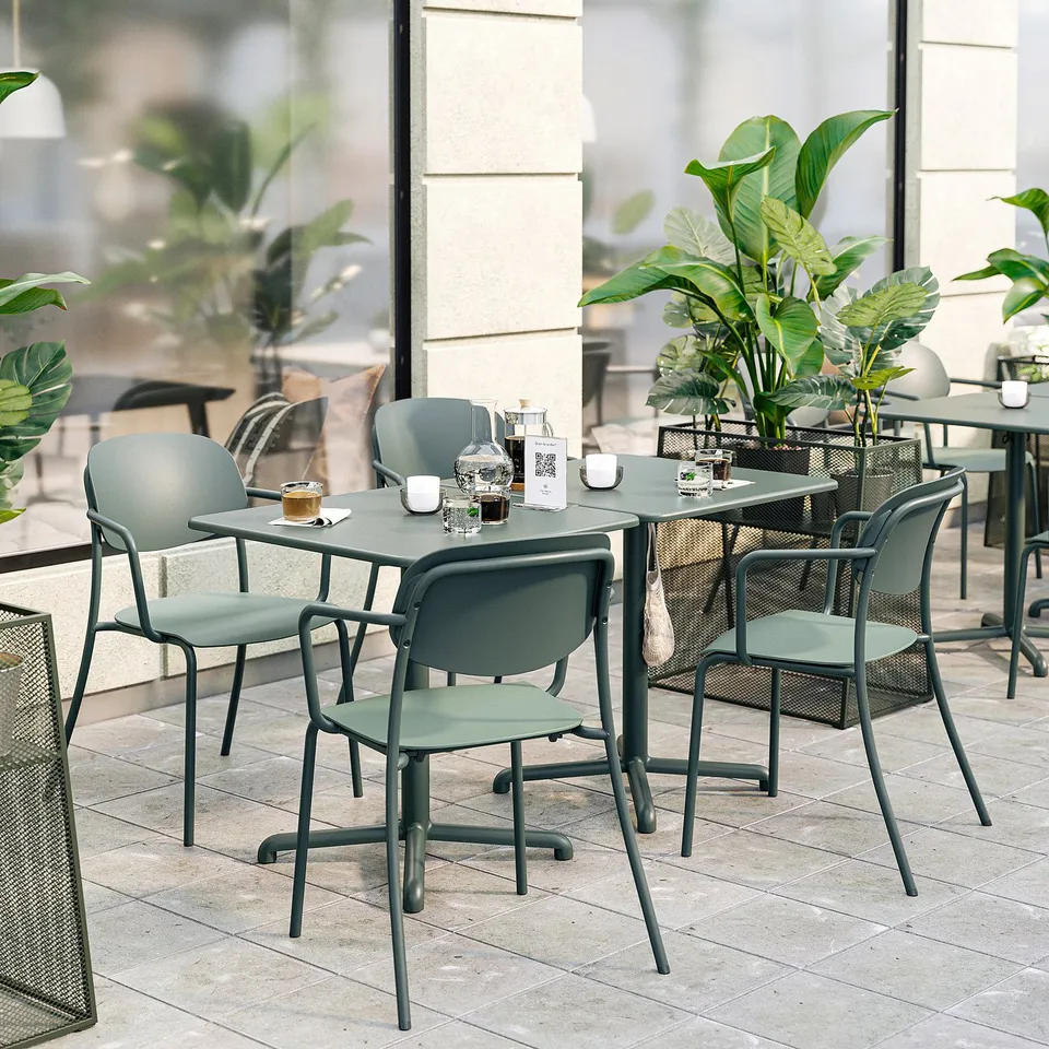 Modern outdoor dining set with green metal tables and chairs, cushioned seats, surrounded by plants.
