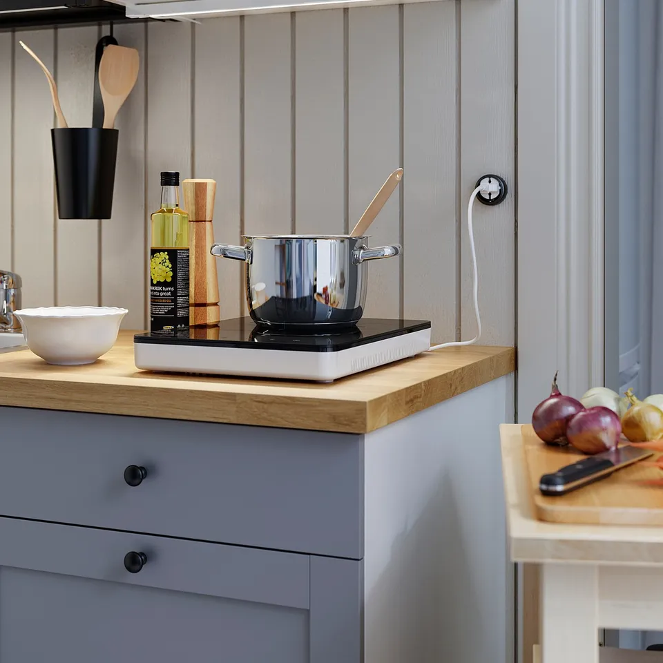 Modern kitchen counter with a single induction burner, stainless pan, wooden utensils, white bowl, and onions.