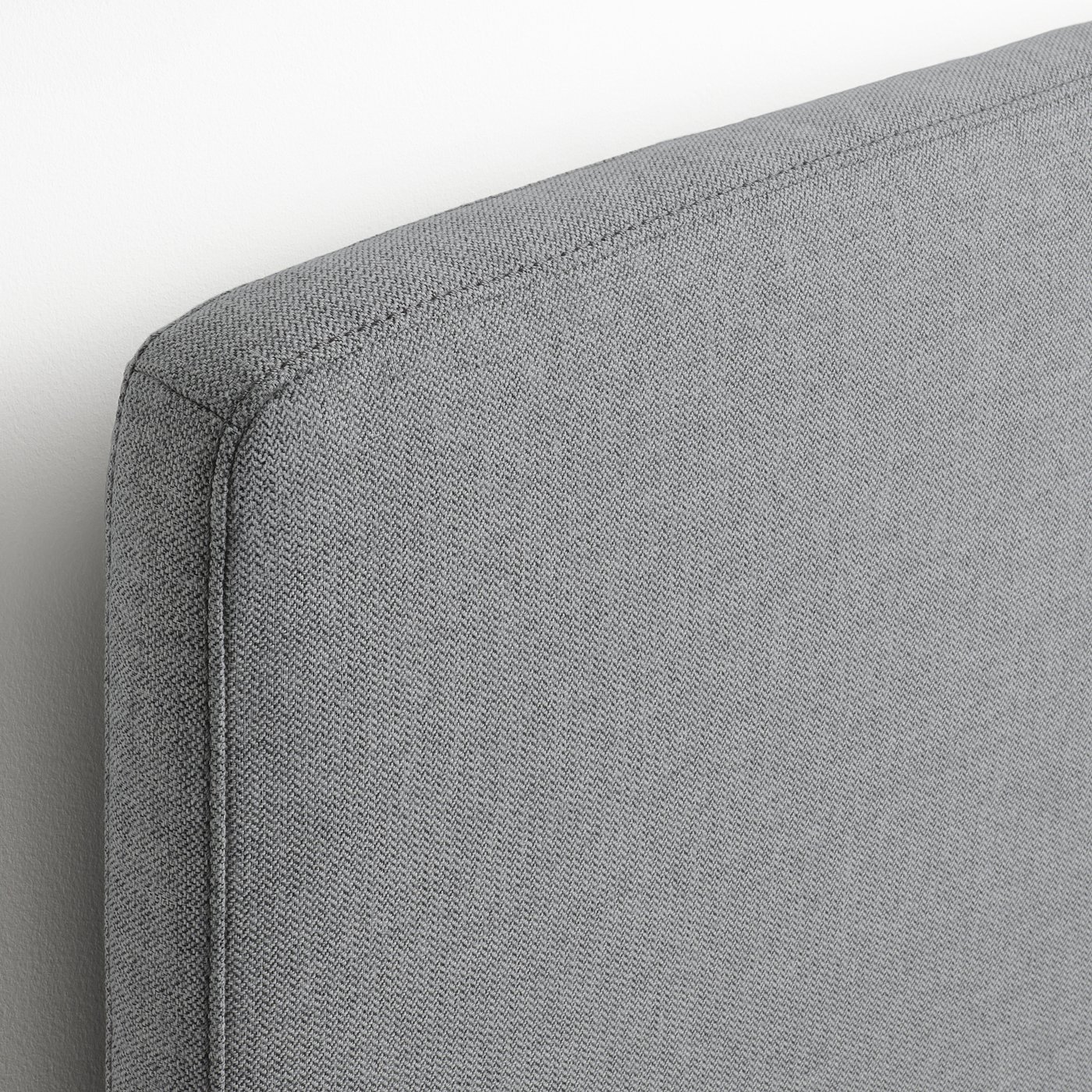 Close-up of neatly upholstered bed frame, showcasing soft, herringbone-patterned fabric and precise stitching.