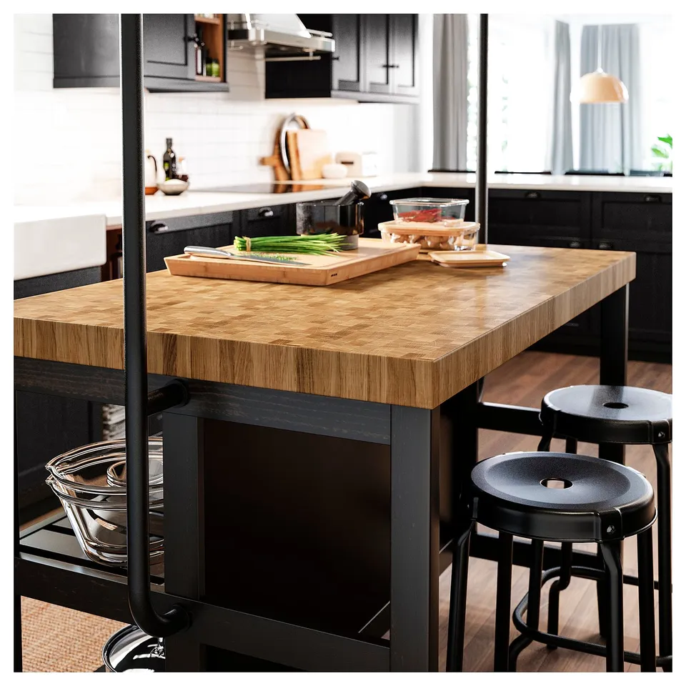 A modern kitchen with a VADHOLMA black and oak wooden island. It a butcher block top, black stools, bowls, and cutting boards.