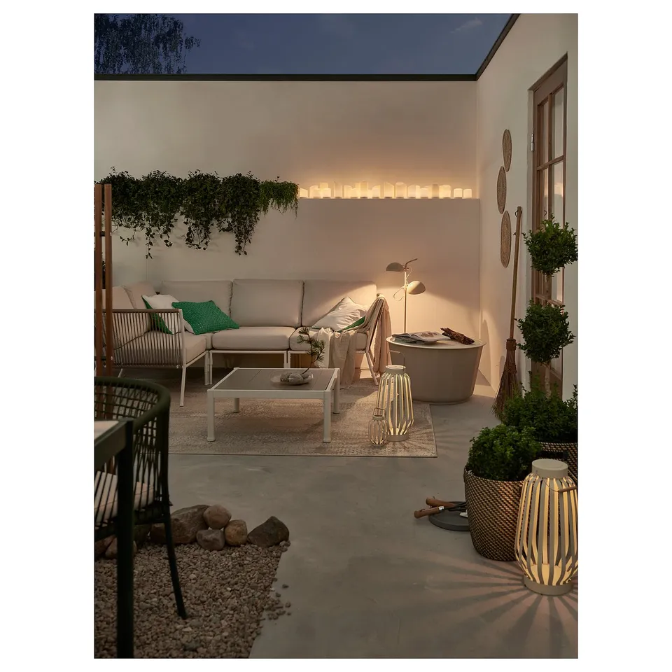 Modern patio with cream sofa, green cushions, white table, bamboo lanterns, plants, and candles.