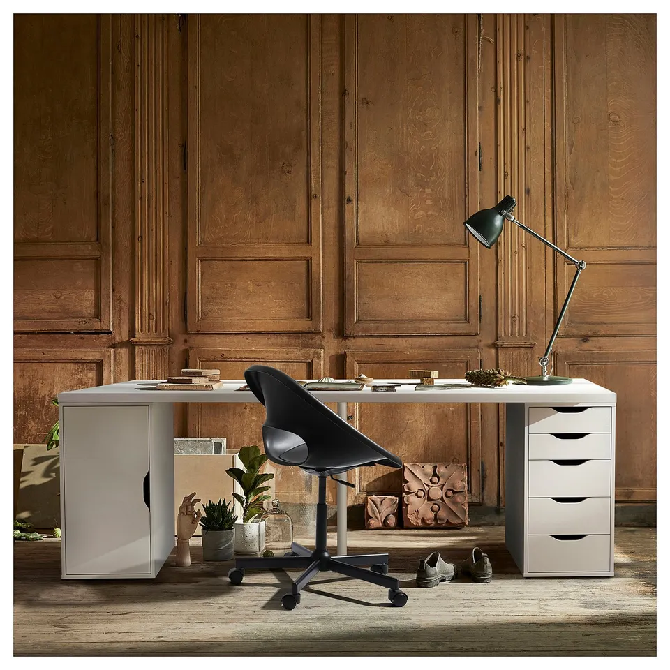 Modern home office with LAGKAPTEN white desk, black chair, wooden panel walls, green lamp, and storage units.