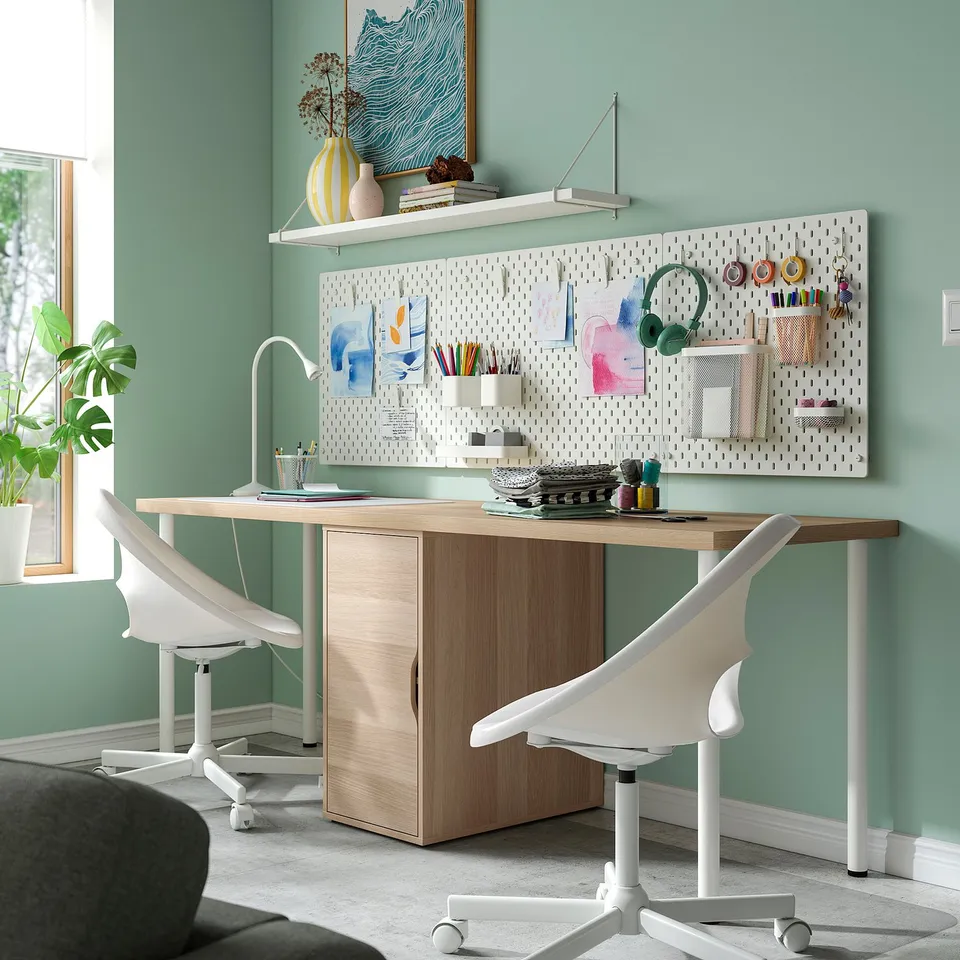LAGKAPTEN corner desk with white legs, light wood top & cabinet, green wall, pegboard storage, practical & stylish home office setup.