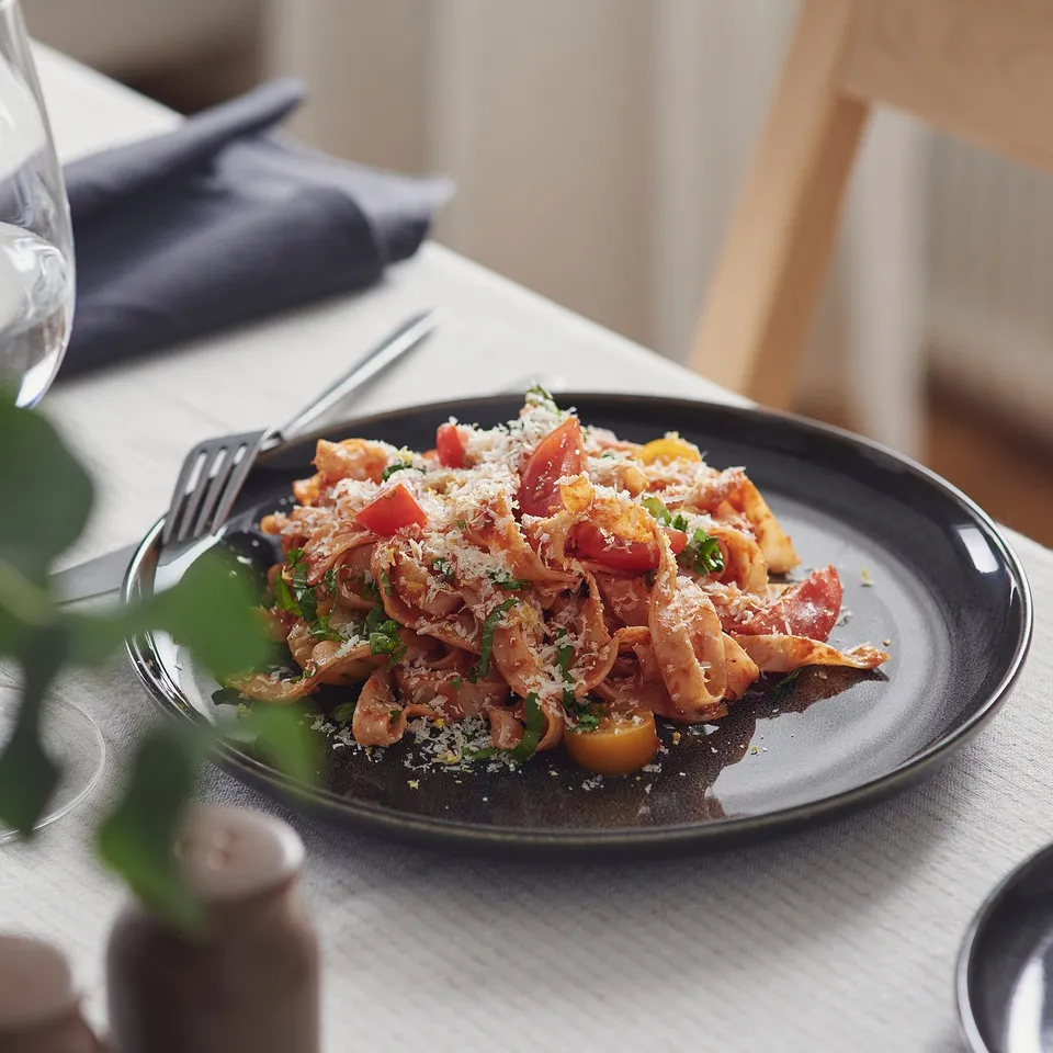 A plate of pasta with tomatoes and cheese. Stoneware with a unique, reactive glaze sits on a table with cutlery and a wine glass.