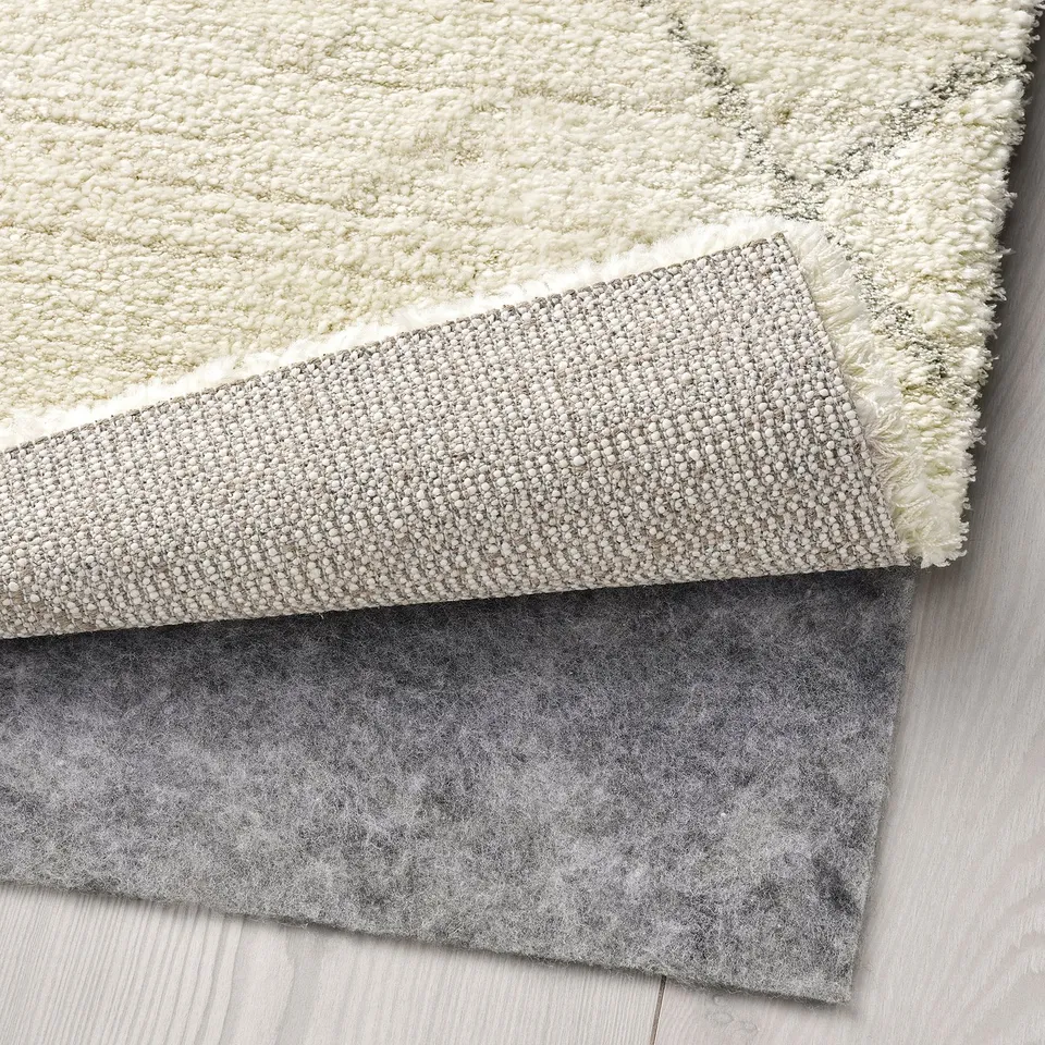 A corner shot of a beige rug with visible underside, featuring a grey non-slip underlay, demonstrating its layered design and soft texture.