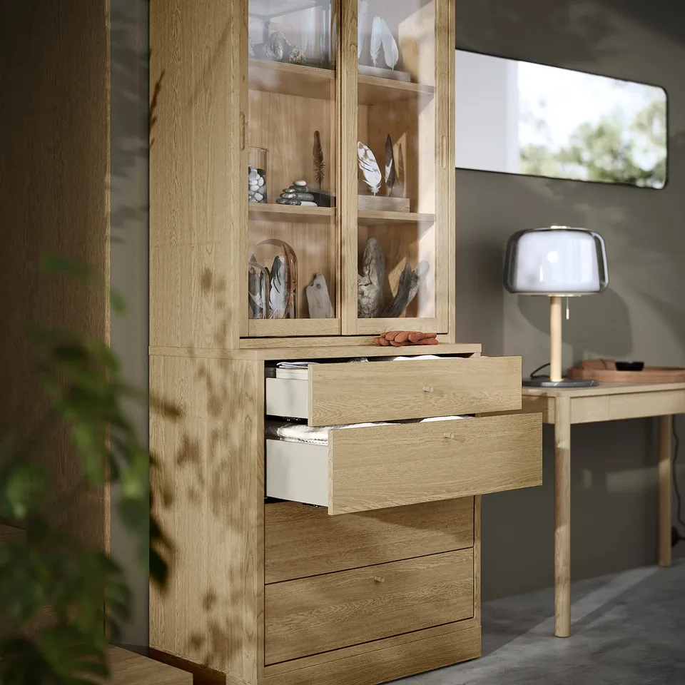 Light wood cabinet with open drawers, displaying various decorative items on shelves and interior drawers.
