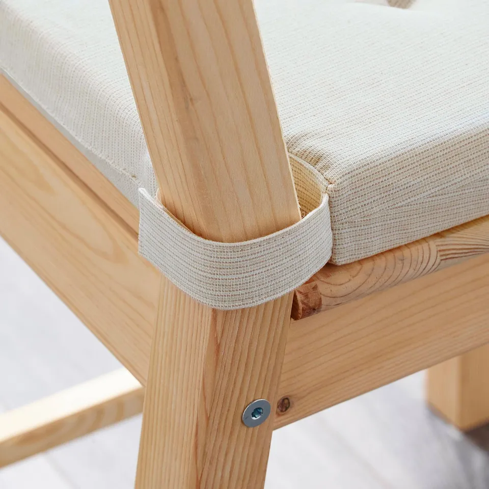 Close-up of a wooden chair with a beige cushion. The cushion has velcro attachments, securing it to the chairs frame.