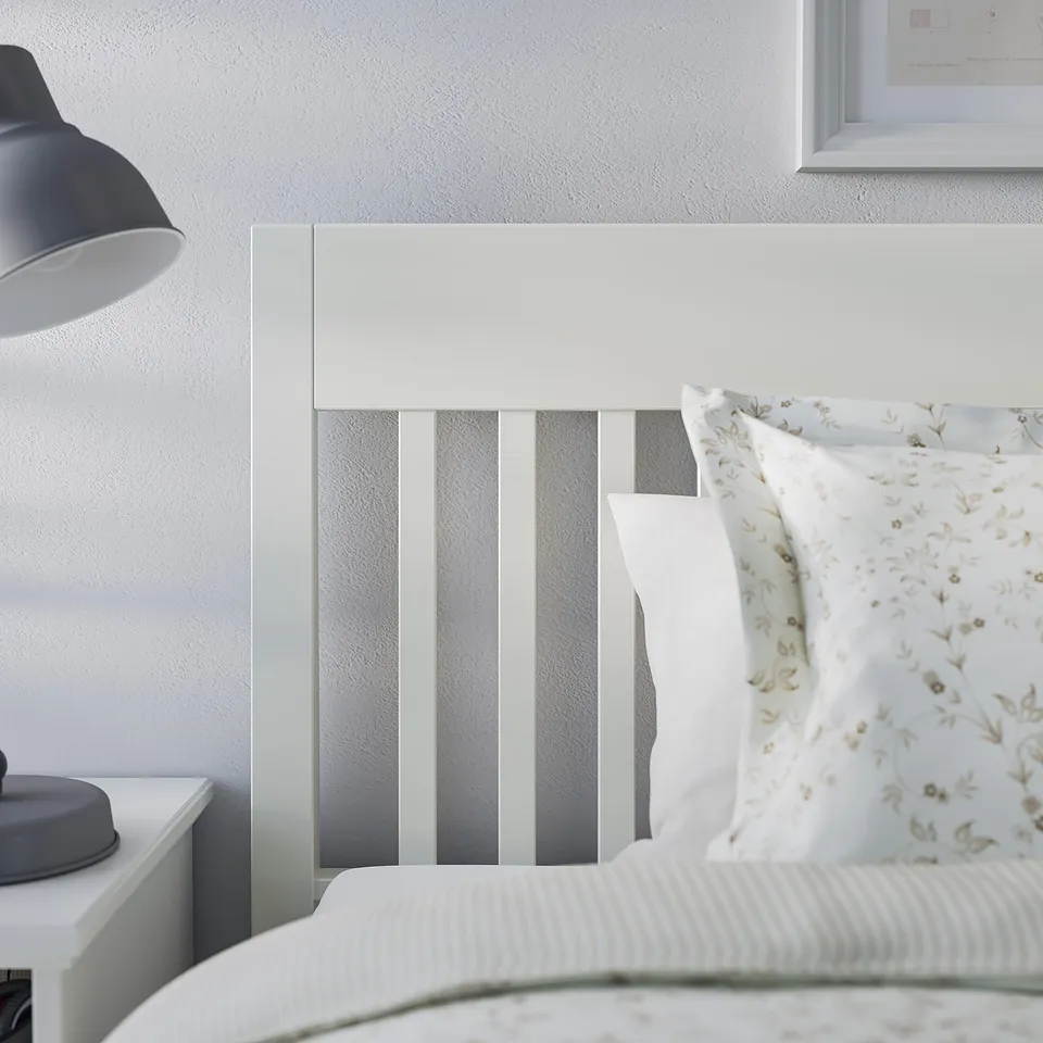A modern white IDANÄS bed frame with a striped headboard. It a decorative pillow and a simple bedside lamp.