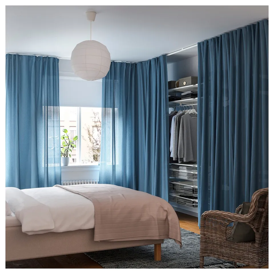 Bedroom with blue curtains, white bed, hanging light, and wicker chair.