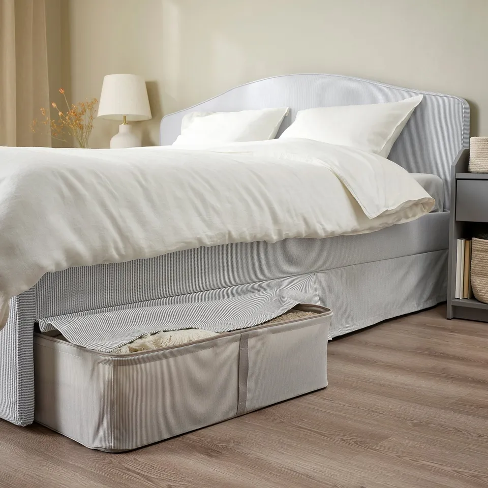 Neat bed with clean linens, padded headboard, and under-bed storage. Grey and white striped cover, ideal for tidy spaces.