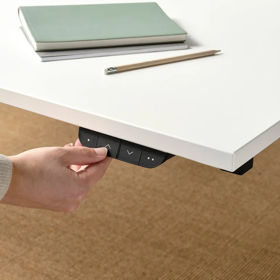 Hand holds control panel, adjusting sit/stand desk height, enhancing focus and comfort.