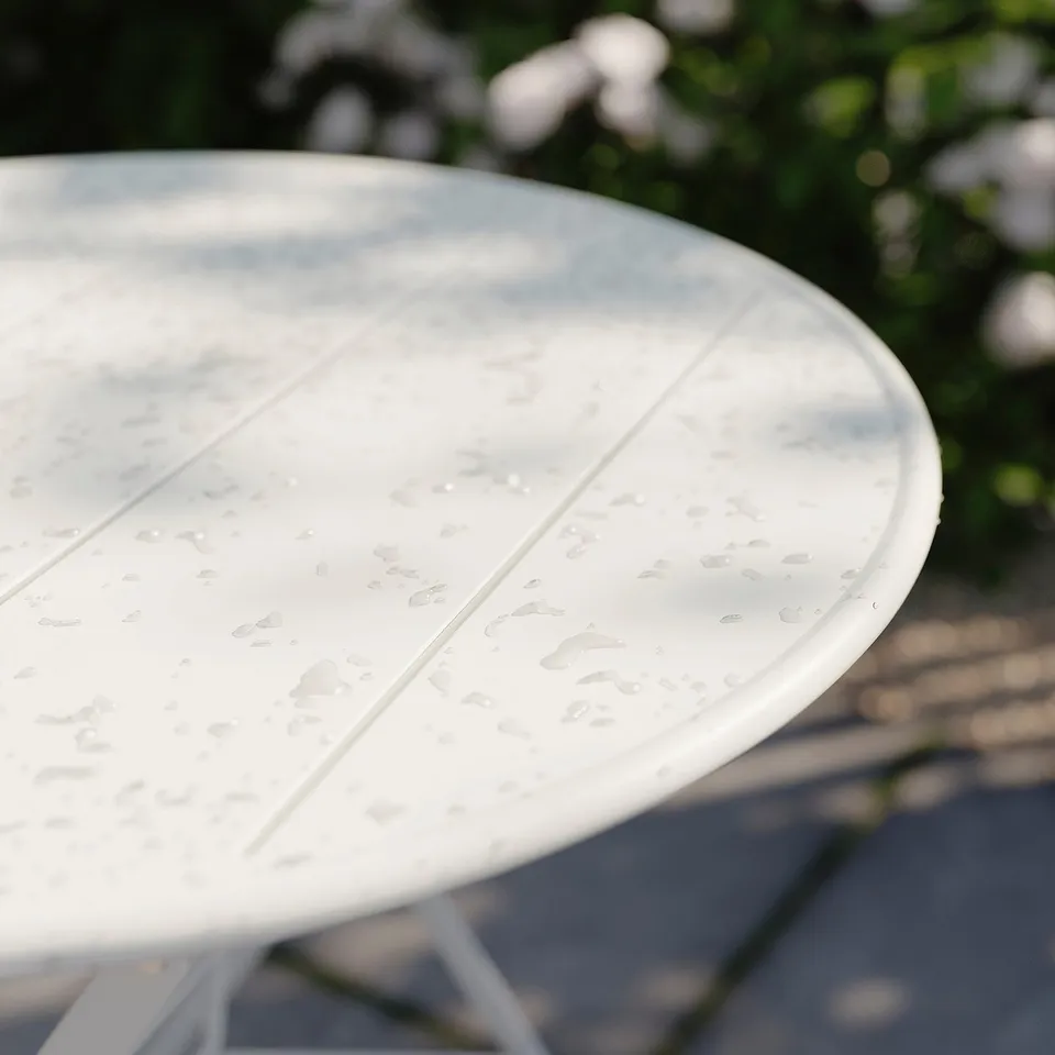 A white, round SUNDSÖ table top with water droplets, made of powder-coated steel, designed for outdoor use.