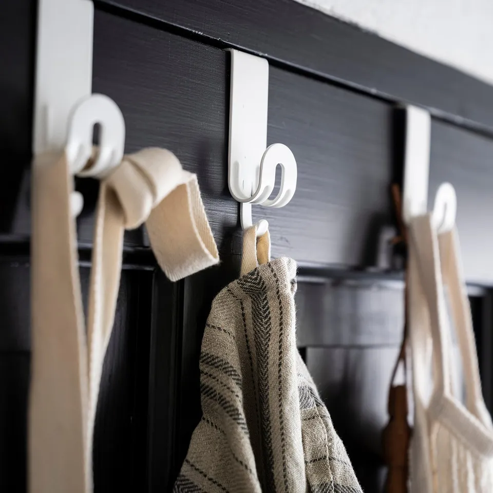 White hooks hang over a black door, holding beige towels. Simple and functional.