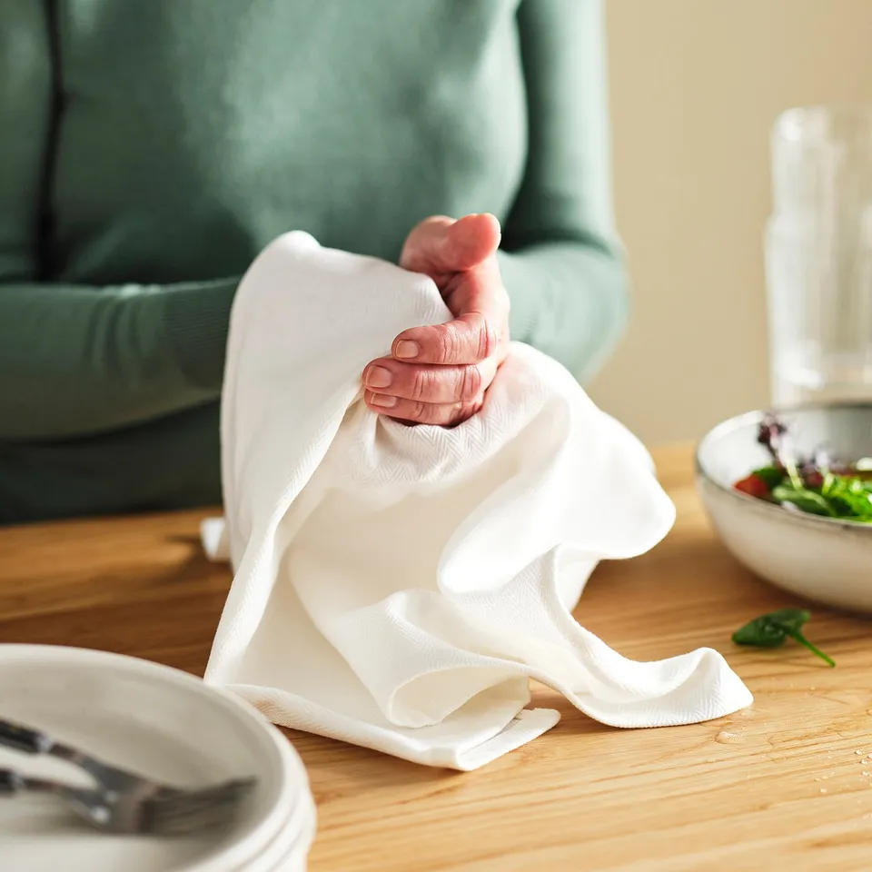 Person holding a white cloth near a table with bowls and utensils.