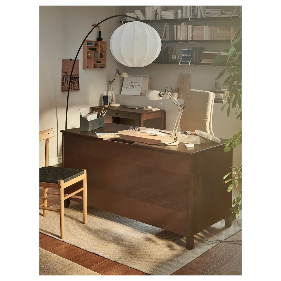 Home office setup with a dark brown wooden desk, chair, lamp, and shelves full of books.