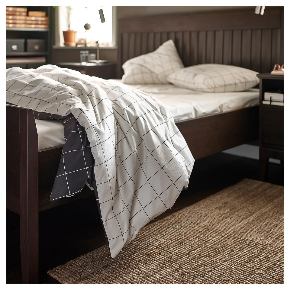 A cosy bedroom with a wooden bed, white grid-patterned blanket, and beige jute rug.