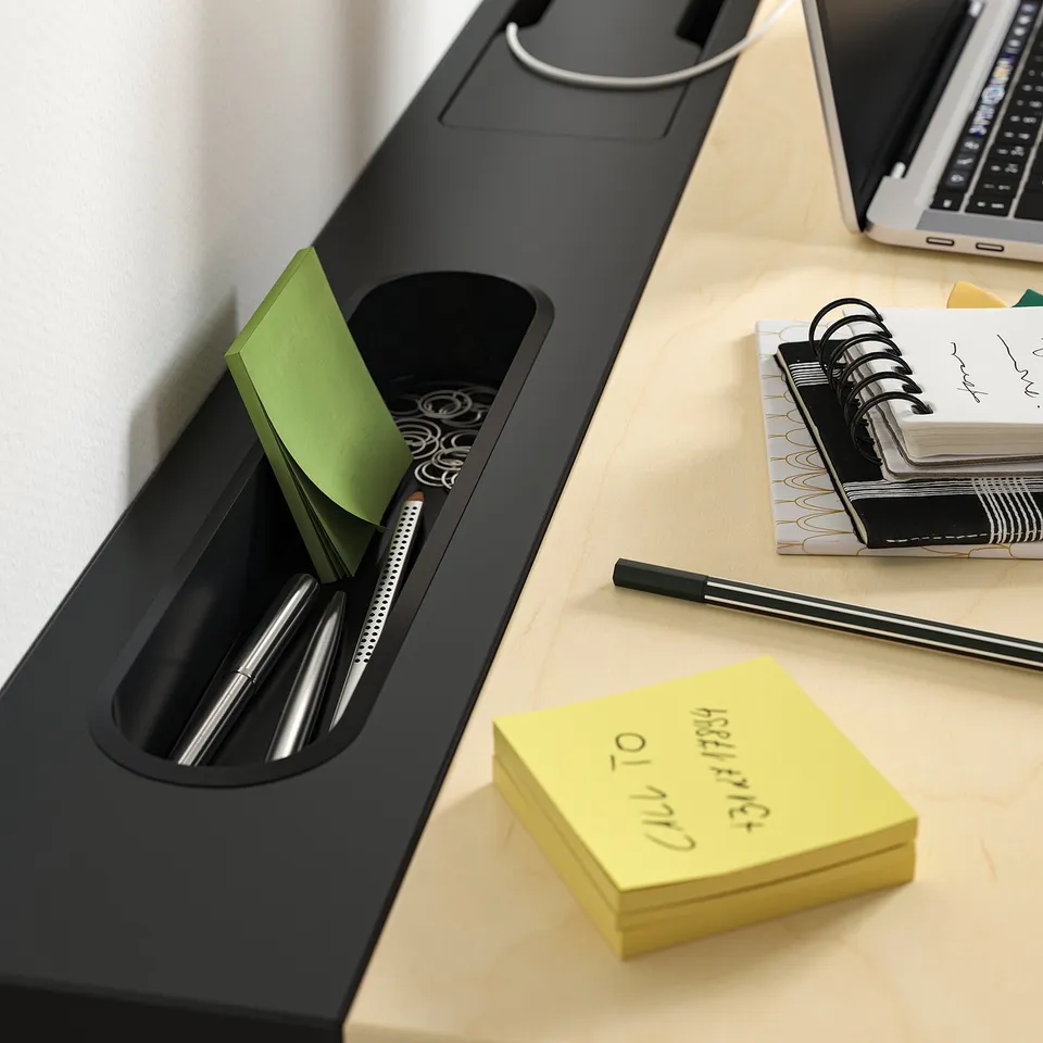 Black desk organiser with pens, post-it notes, and a laptop.