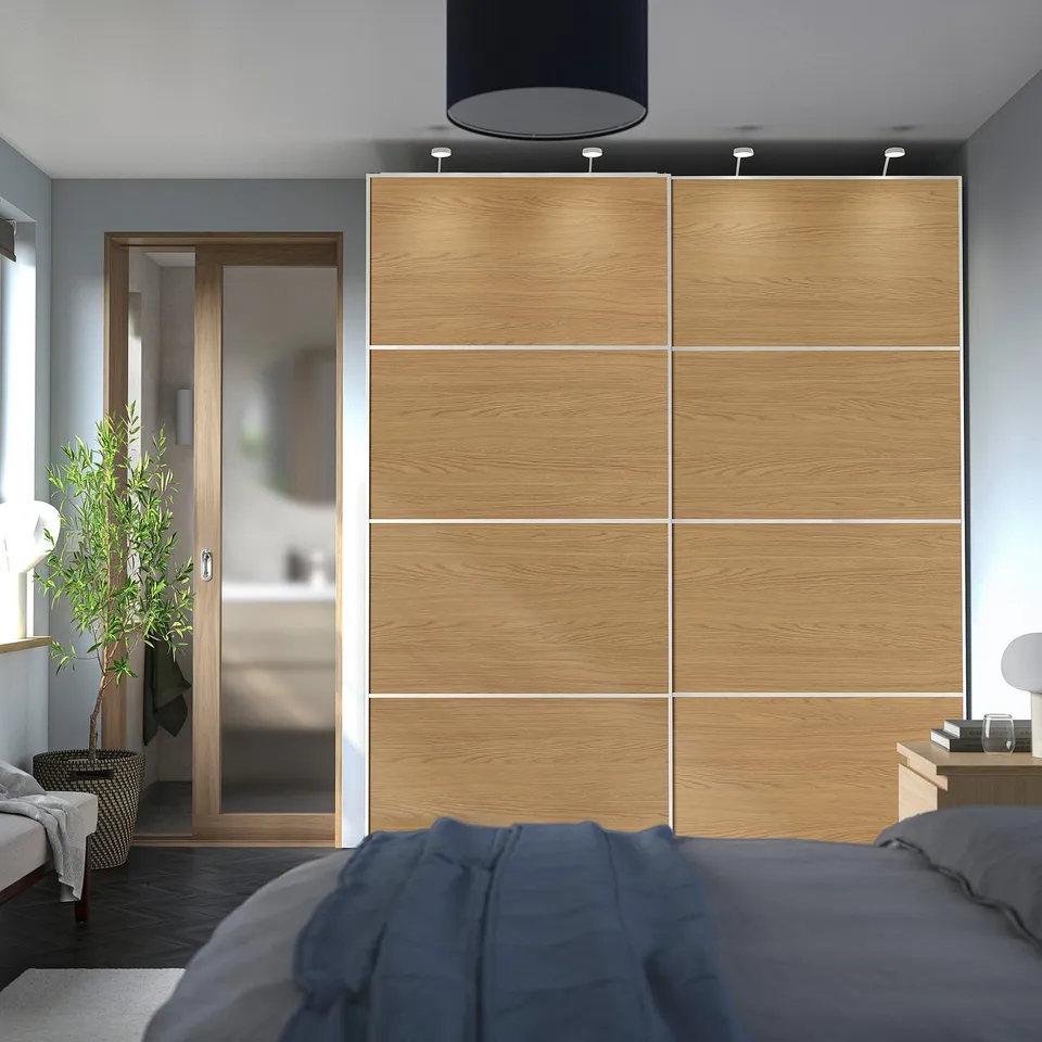 Two large MEHAMN wardrobes with oak panels in bedroom, dark and light woods. Bed with blue blanket, sliding glass door.