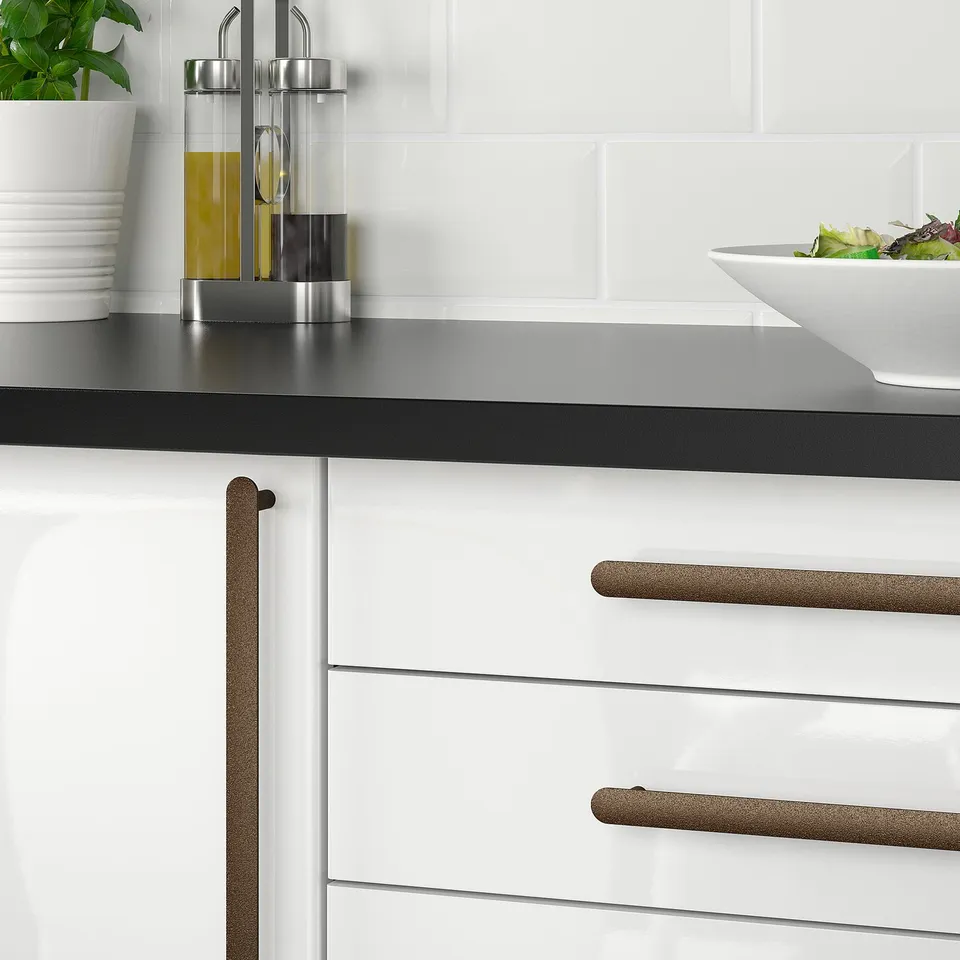 Modern kitchen with white cabinets, black countertop, and silver knobs. Counter has oil bottles and a bowl.