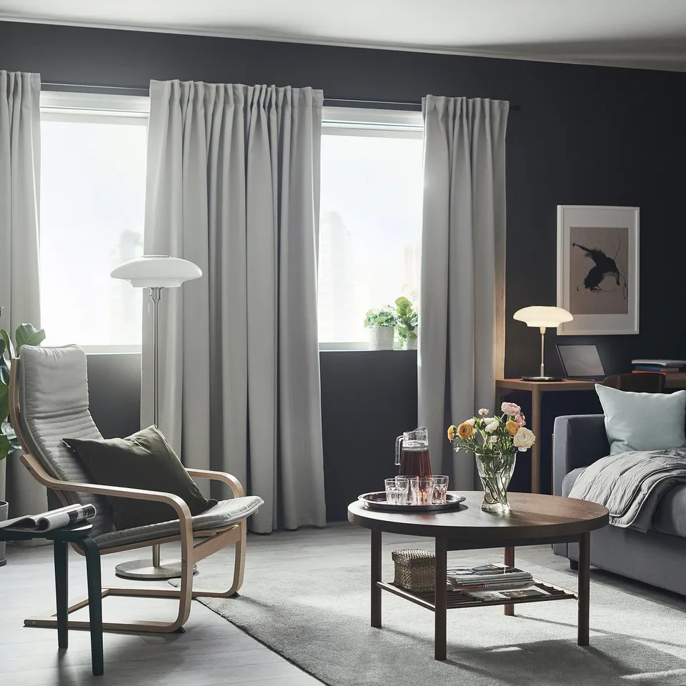 Modern living room with MAJGULL dark grey curtains, cosy armchair, coffee table, and desktop setup.