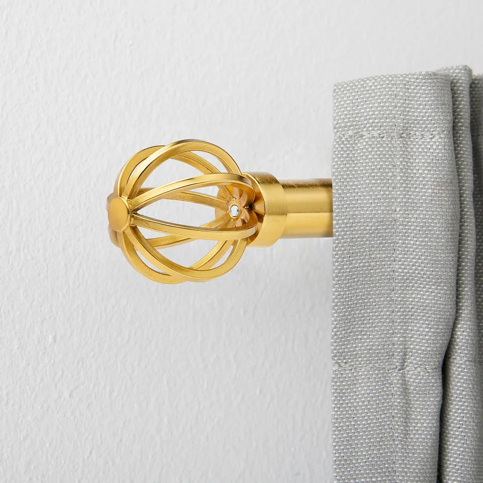 Golden decorative curtain rod finial with intricate design, holding light grey curtain.