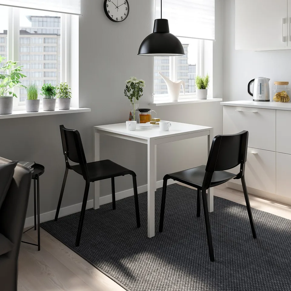 Modern kitchen with white table, black stackable chairs, grey rug.