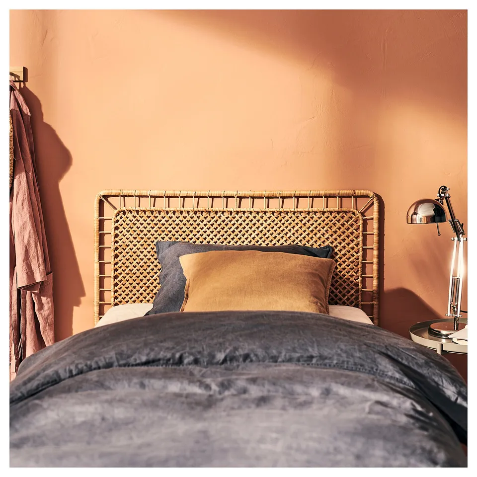 Bed with wicker headboard, warm pillows, peach walls, wooden side table with lamp.