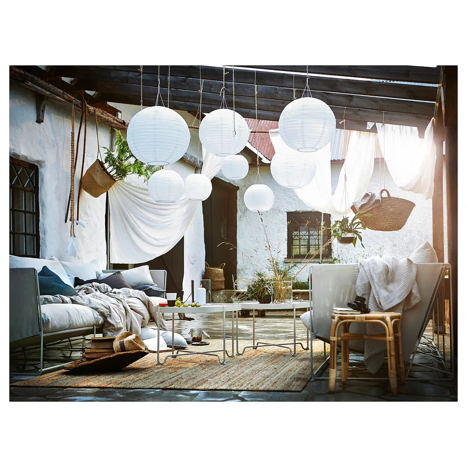 Outdoor patio with white hanging SOLVINDEN lamps, comfortable seating, rug, plants, and blankets.