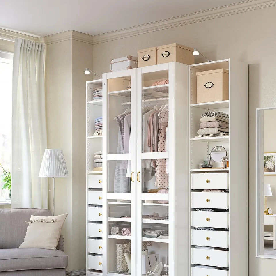 A white PAX wardrobe organises clothes and accessories, featuring glass and solid drawers.