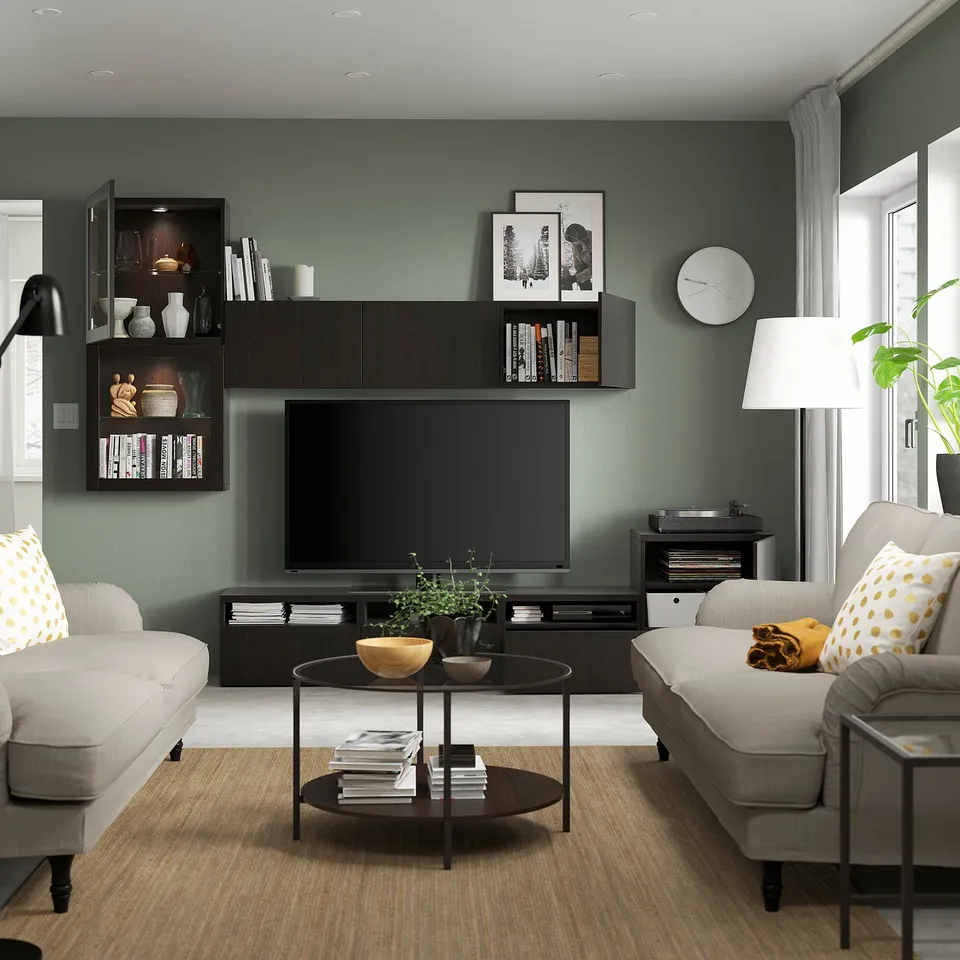 Modern living room with green walls, tv, two sofas with yellow pillows, coffee table with items, record player, and floor lamp.
