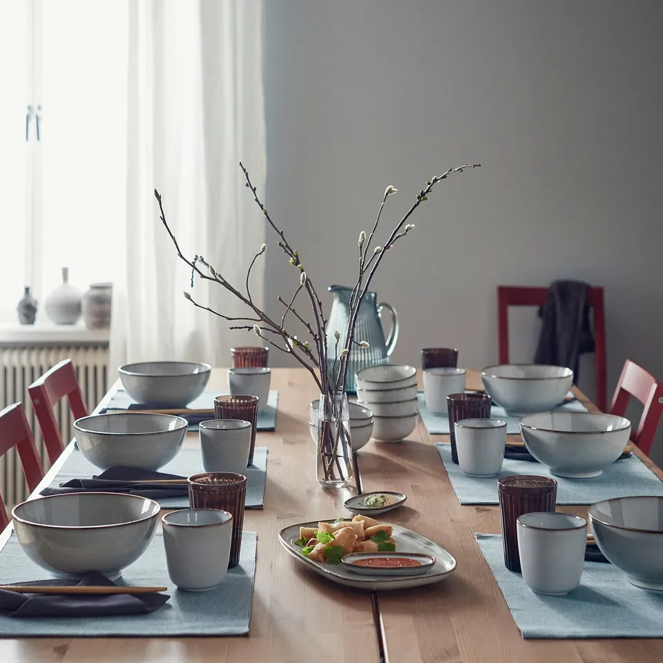 Sandy-glazed GLADELIG tableware set on rustic table with red chairs and branch centrepiece.