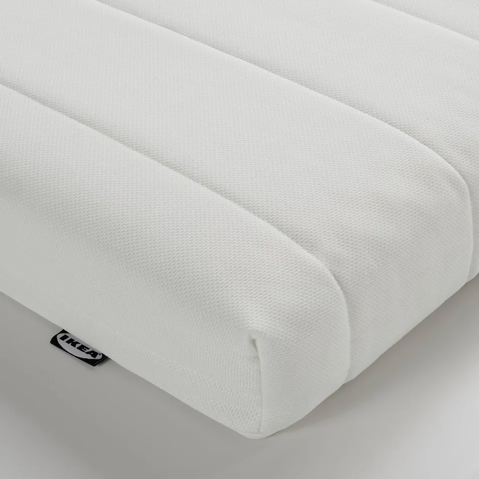 Close-up of a white foam mattress corner, showcasing textured surface and quality material. Ikea logo visible.
