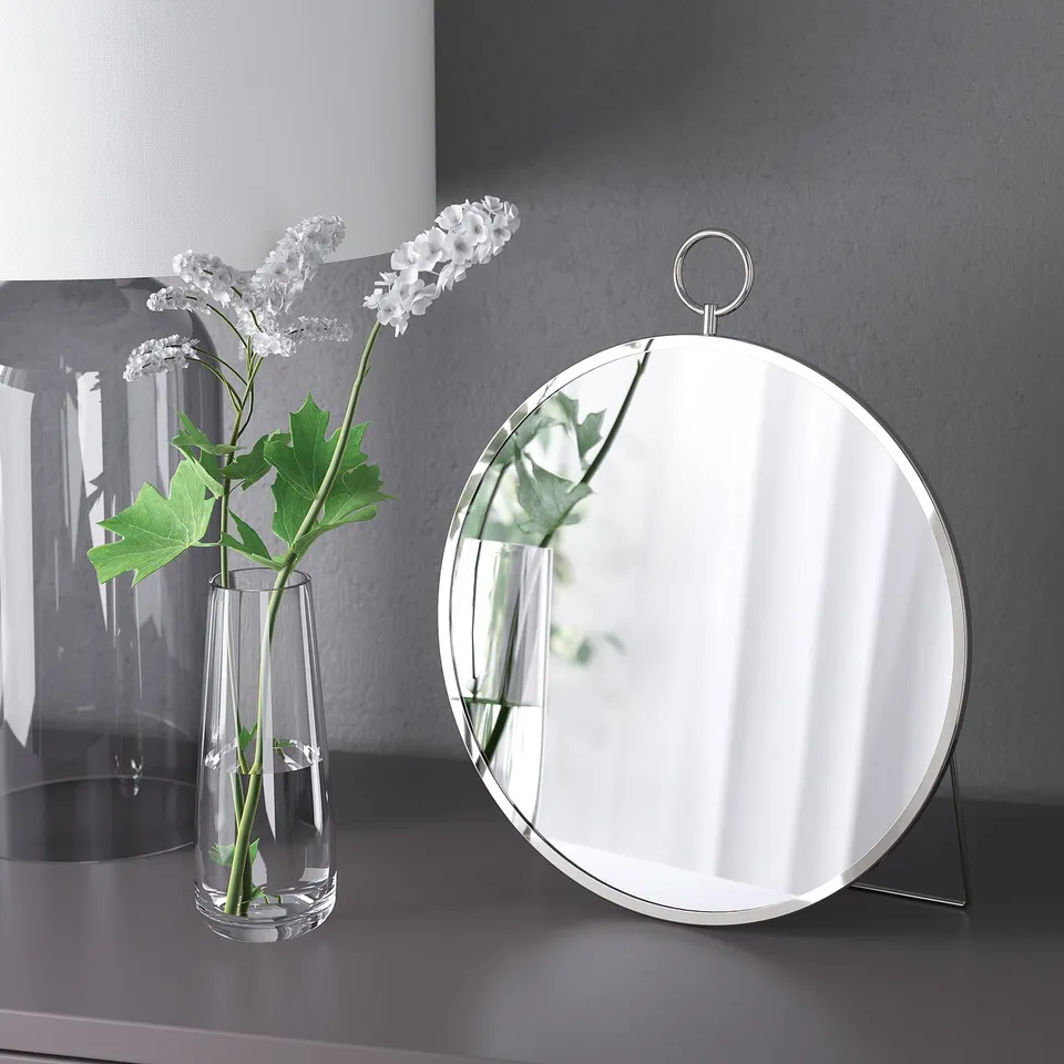 Mirror propped on stand next to glass vase with white flowers.