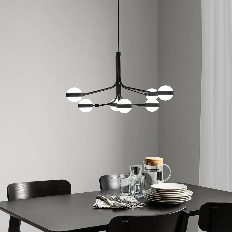 Modern black chandelier with 8 lights hangs above a dining table with dishes, adding stylish functionality.