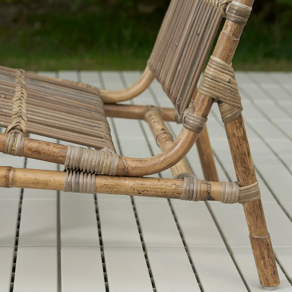 Wicker patio chair on tiled deck. Crafted with rattan and stainless steel joints, showcasing sturdy, detailed handiwork.
