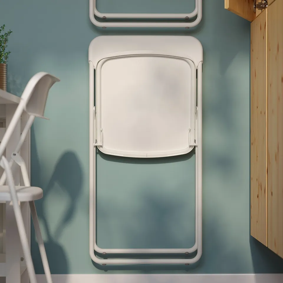 Foldable dining chair mounted on wall, shown in white, ready for space-saving storage.