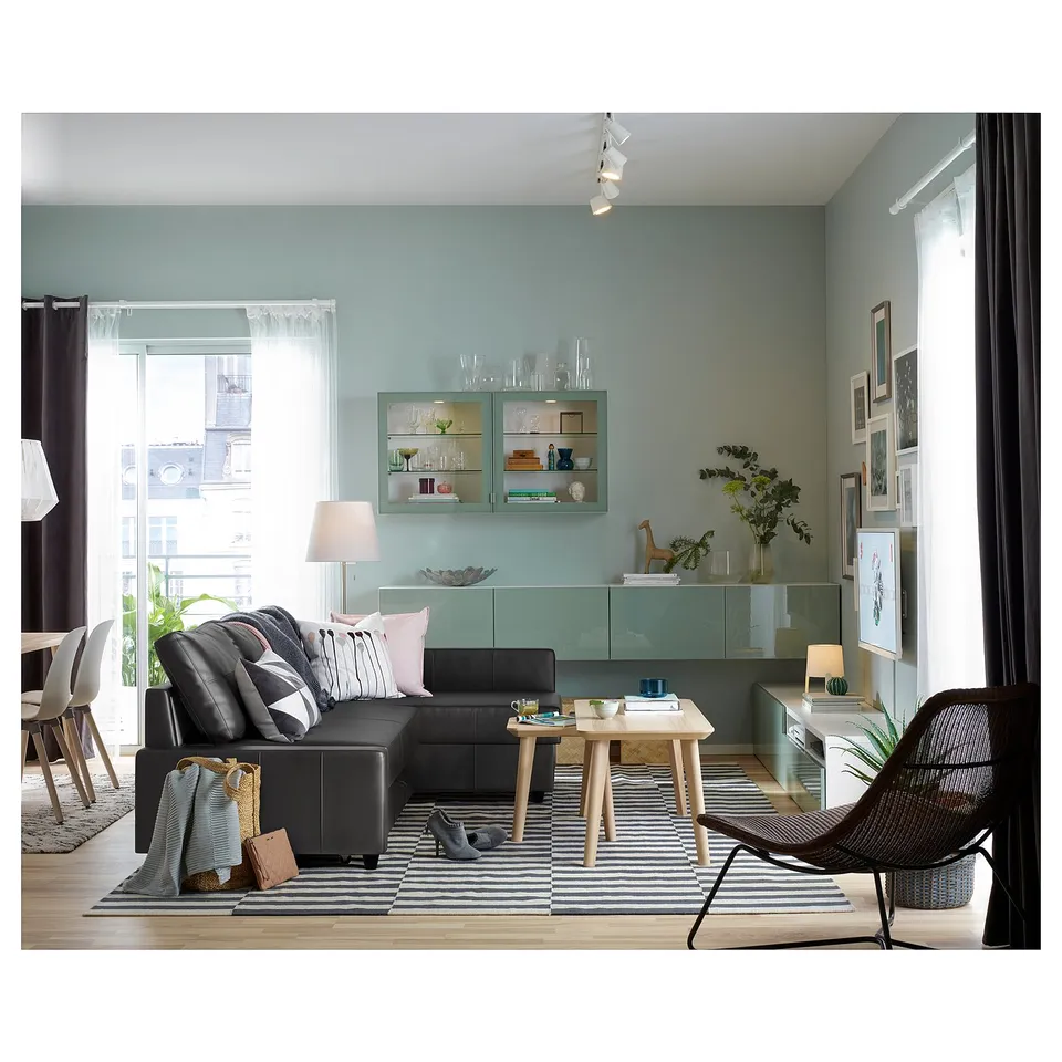 Modern living space with light blue walls, black sofa, striped rug, wooden table, and shelves with decorative items.