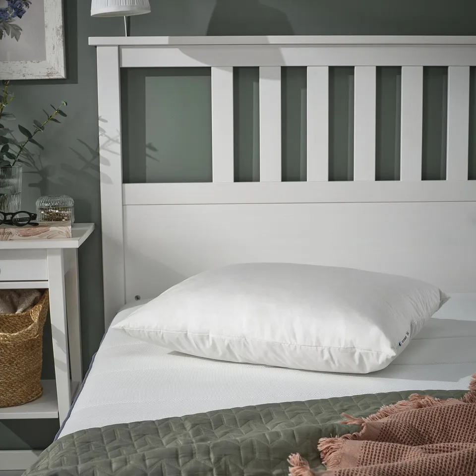 White PILSPINNARE pillow on bed with green headboard, ideal for stomach sleepers, next to basket and jar.